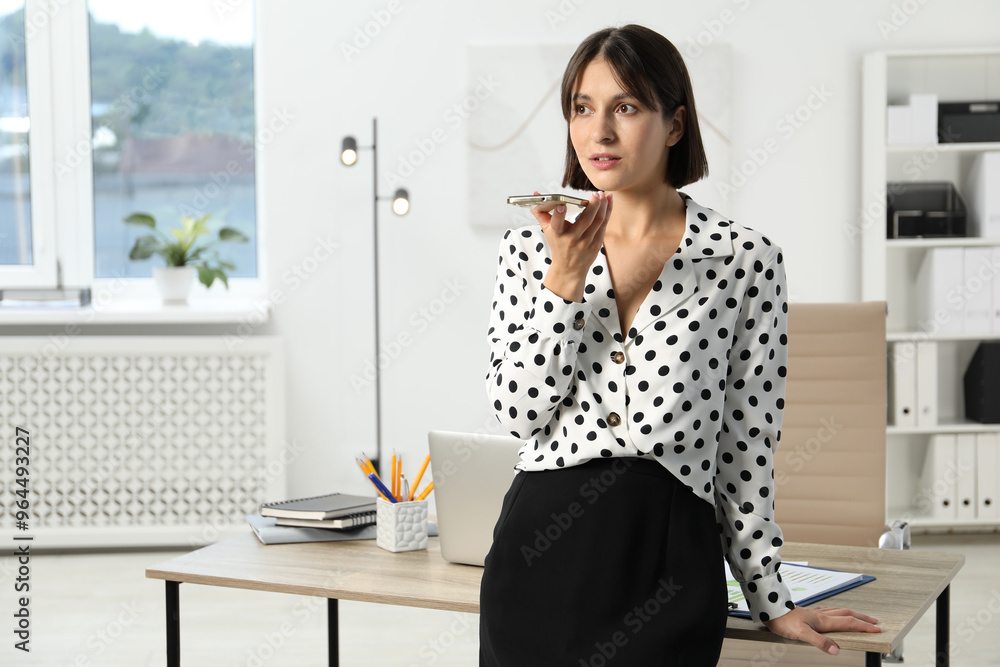 Beautiful woman recording voice message via smartphone in office Beautiful woman recording voice message via smartphone in office