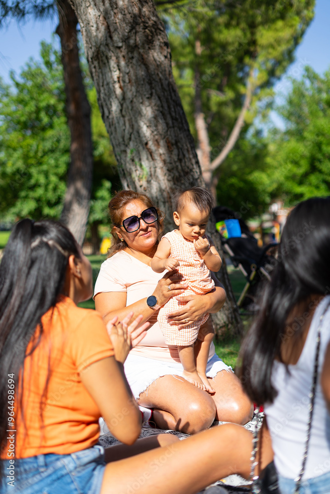 Latin family of young grandmother with her two daughters and baby granddaughter having picnic at outdoors Latin family of young grandmother with her two daughters and baby granddaughter having picnic at outdoors