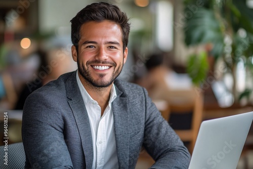 Smiling confident businessman working on laptop in modern office with natural light and plants, professional portrait 