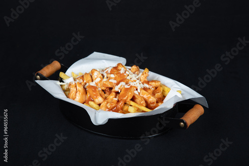 Gourmet Poutine-Style Fries: Crispy Potatoes with Rich Sauce and Cheese on White Paper, Served in Black Dish with Wooden Handles, Dark Background.