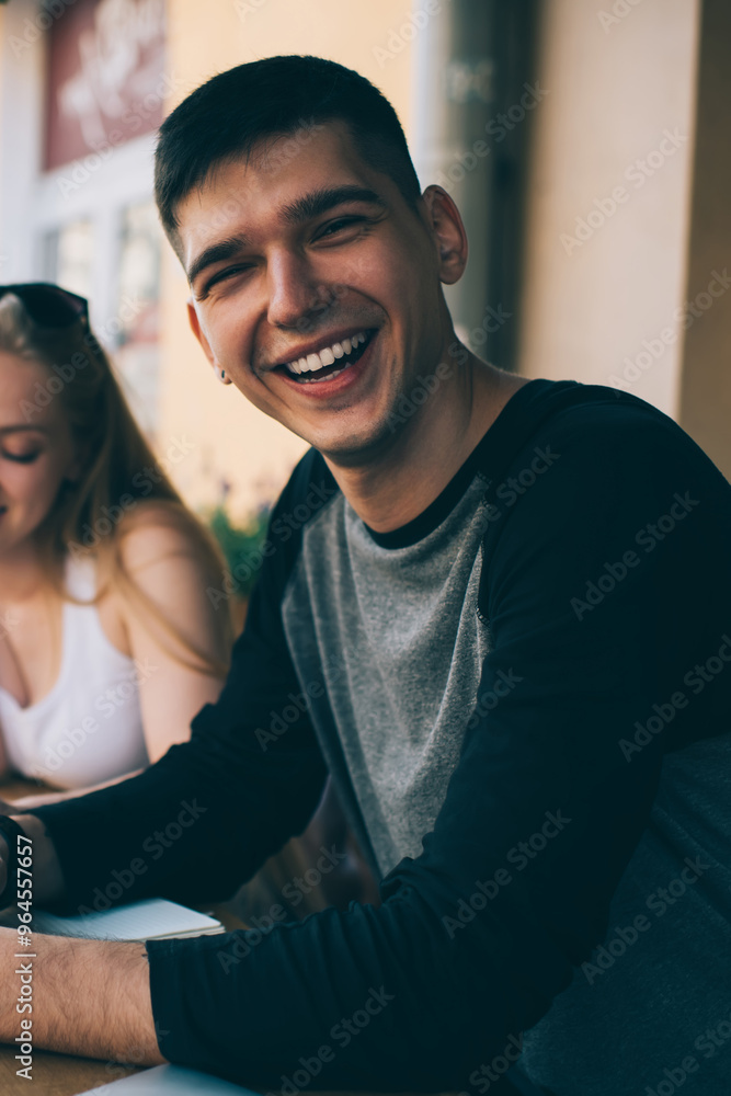 Obraz premium Portrait of cheerful man in casual wear sitting in street cafeteria with female students spending time for private lesson on leisure, positive male smiling at camera while girlfriend near planning day
