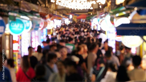Blurred silhouettes, crowd people walking through busy street market, slow motion shot. Local and foreign tourists stroll at Haeundae Traditional Market, exploring food stalls and enjoying vibe