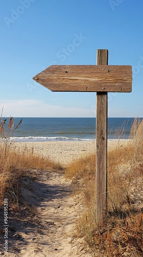 Wooden arrow sign points toward a sandy path leading to the ocean. photo