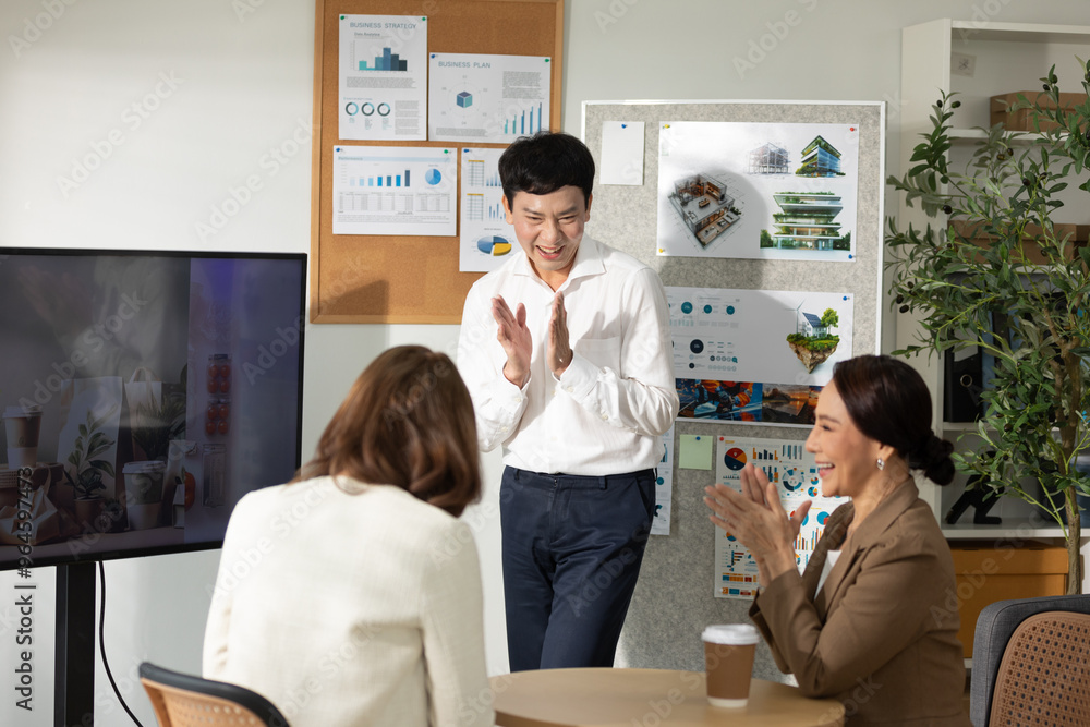 Group of Asian business professionals celebrating successful project during office meeting. Man stands clapping while his colleagues join in, creating joyful and positive atmosphere Group of Asian business professionals celebrating successful project during office meeting. Man stands clapping while his colleagues join in, creating joyful and positive atmosphere