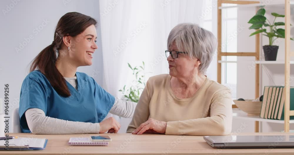 Portrait of a senior elderly gray-haired woman patient in medical office talking to a female friendly nurse sitting at the desk in clinic and having consultation during exam. 4k video. Portrait of a senior elderly gray-haired woman patient in medical office talking to a female friendly nurse sitting at the desk in clinic and having consultation during exam. 4k video.