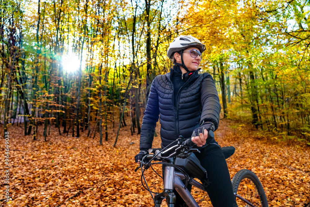 Φωτογραφία Portrait of middle aged woman wearing black sporty jacket, black cycling pants and white bike helmet standing with bicycle in forest in autumn scenery