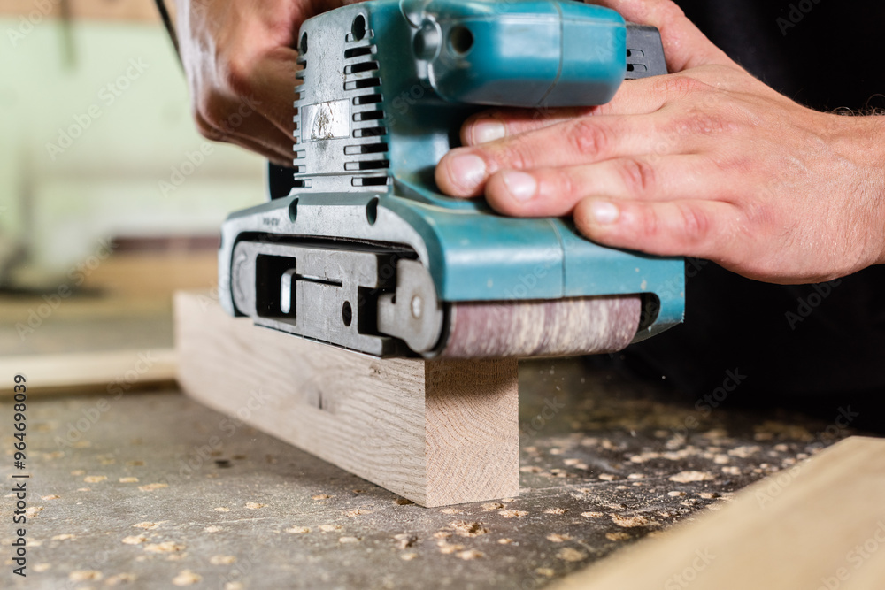 A carpenter grinds an oak plank part with a hand grinder A carpenter grinds an oak plank part with a hand grinder