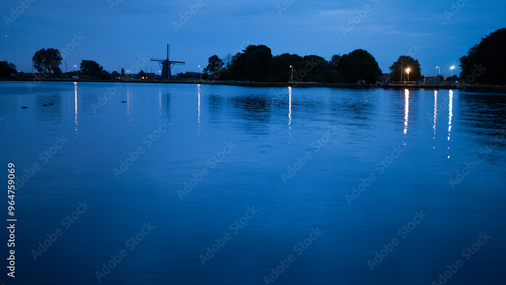 Fototapeta premium Sunset over the river with the mill in the background under the blue sky in Leiden, the Netherlands
