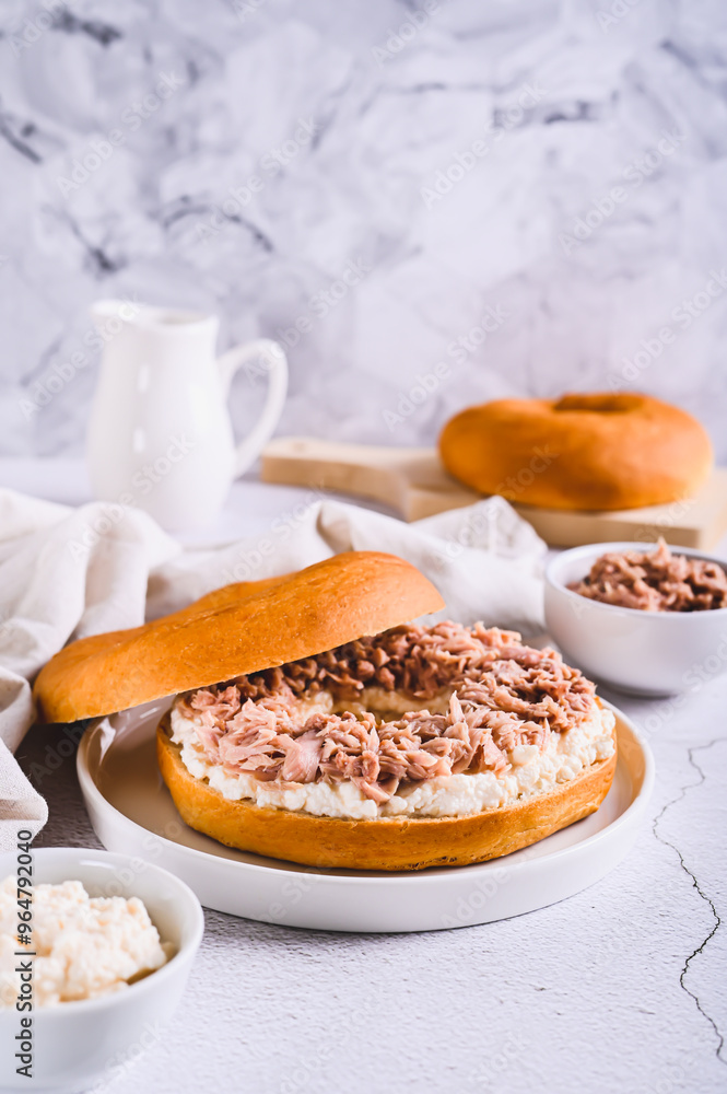 Savory bagel with ricotta and canned tuna on a plate on a table vertical view Savory bagel with ricotta and canned tuna on a plate on a table vertical view