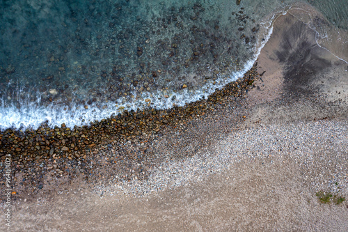 Drone Cenital view: Sea foamy waves splashing against the rocky coast at sunrise