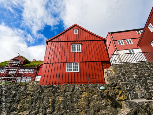 Scandinavian red buildings set against atop a hill. Stone foundation next to the North Atlantic Ocean. Located in Old Town Tórshavn, the capital city of the Faroe Islands on the island of Streymoy.