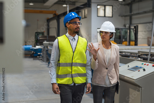 Indian female factory manager introducing the production line to a recruit, an African American worker, and congratulating him on a new job, front view. photo