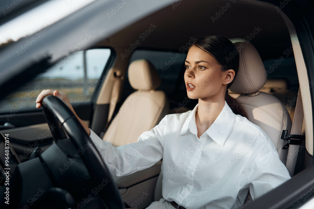 A woman with an open mouth, wearing a white shirt, is sitting in the driver's seat of a car, one hand on the steering wheel, capturing a candid moment of surprise or conversation A woman with an open mouth, wearing a white shirt, is sitting in the driver's seat of a car, one hand on the steering wheel, capturing a candid moment of surprise or conversation