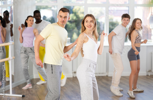 Slim young man and woman practicing active dance in training hall during group dancing classes