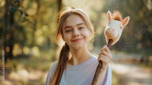 Cheerful girl enjoying hobby horsing with toy horse in a bright sunny park surrounded by greenery photo