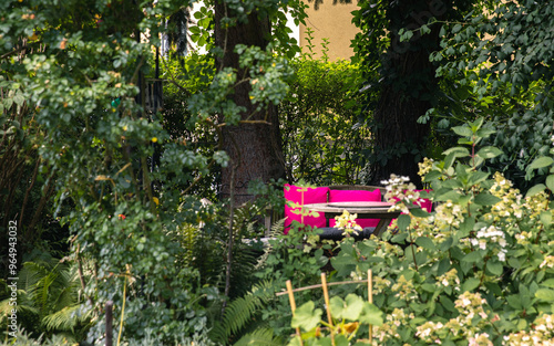 Fototapeta Cozy park bench with pink blanket surrounded by lush green plants, trees, vibran