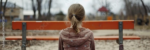 A young girl sits alone on a friendship bench, waiting hopefully for a playmate to join her on the playground. photo