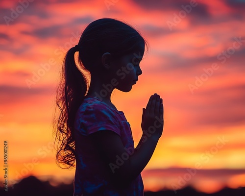 Silhouette of girl child with clasped hands in prayer, vivid sunset or sunrise sky, prayer concept, union, fellowship, and reflection photo