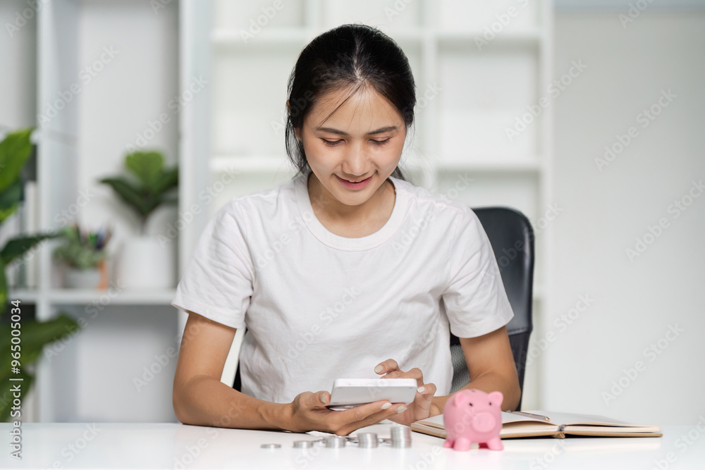 Young Woman Managing financial with Smartphone and Piggy Bank at Home Office Desk Young Woman Managing financial with Smartphone and Piggy Bank at Home Office Desk