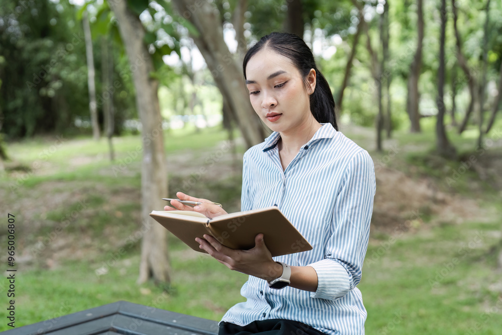 Young Woman Writing in Notebook While Sitting in a Park on a Sunny Day Young Woman Writing in Notebook While Sitting in a Park on a Sunny Day