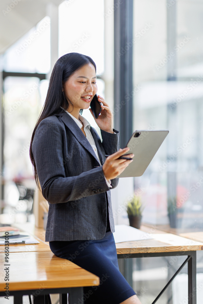 Fototapeta premium Modern business asian woman in formalwear using digital tablet while standing near wooden desk in an office interior in the office. business people concept.