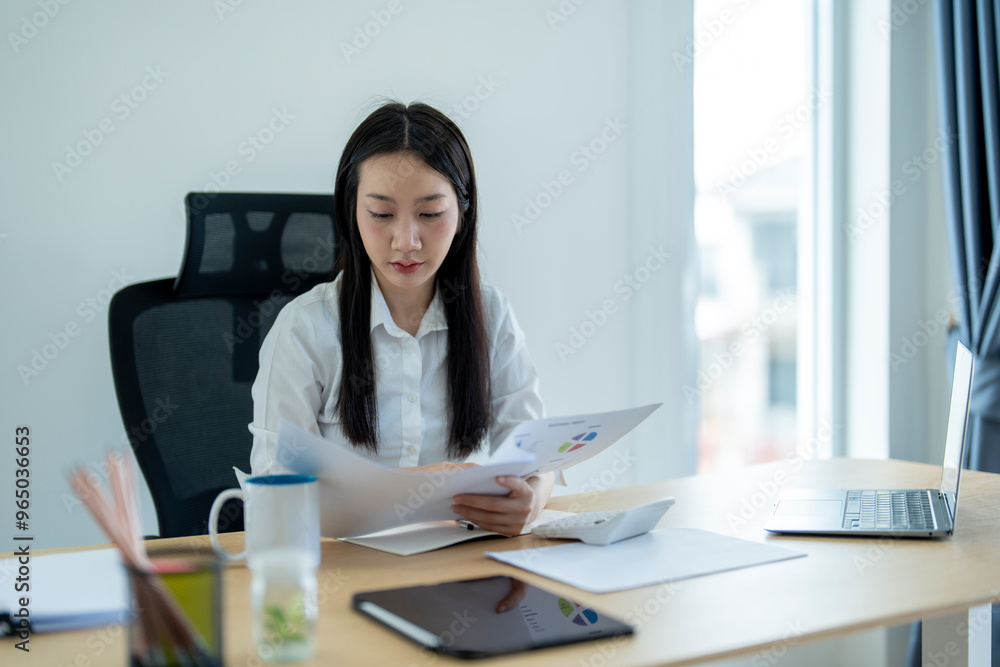 Asian businesswoman reading financial report documents at office desk Asian businesswoman reading financial report documents at office desk