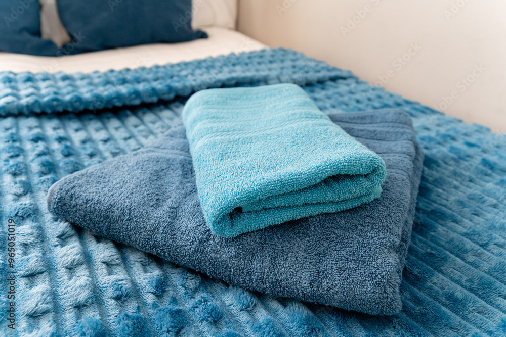 On the bed, there are two soft and inviting blue towels elegantly stacked one on top of the other, adding a vibrant pop of color and a warm, cozy feel to the overall space On the bed, there are two soft and inviting blue towels elegantly stacked one on top of the other, adding a vibrant pop of color and a warm, cozy feel to the overall space