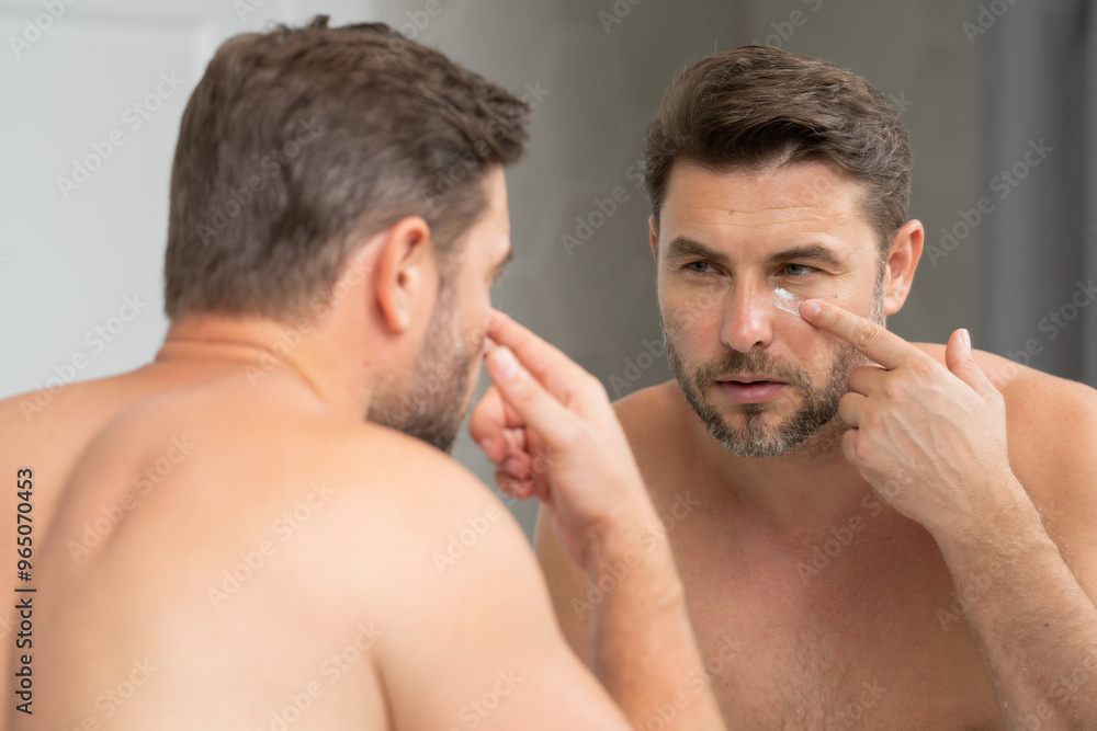 A man is applying lotion to his face in front of a mirror. Concept of self-care and personal grooming A man is applying lotion to his face in front of a mirror. Concept of self-care and personal grooming