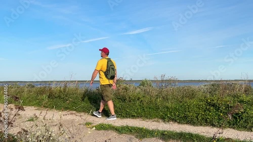 male person walks with a backpack along the road along the sea. The guy is wearing a yellow T-shirt and shorts. weekends, vacations and hobbies concept. walking.