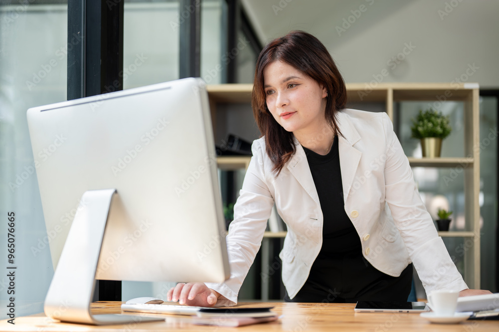 A businesswoman is standing at her desk, typing on a computer keyboard and looking at the screen. A businesswoman is standing at her desk, typing on a computer keyboard and looking at the screen.