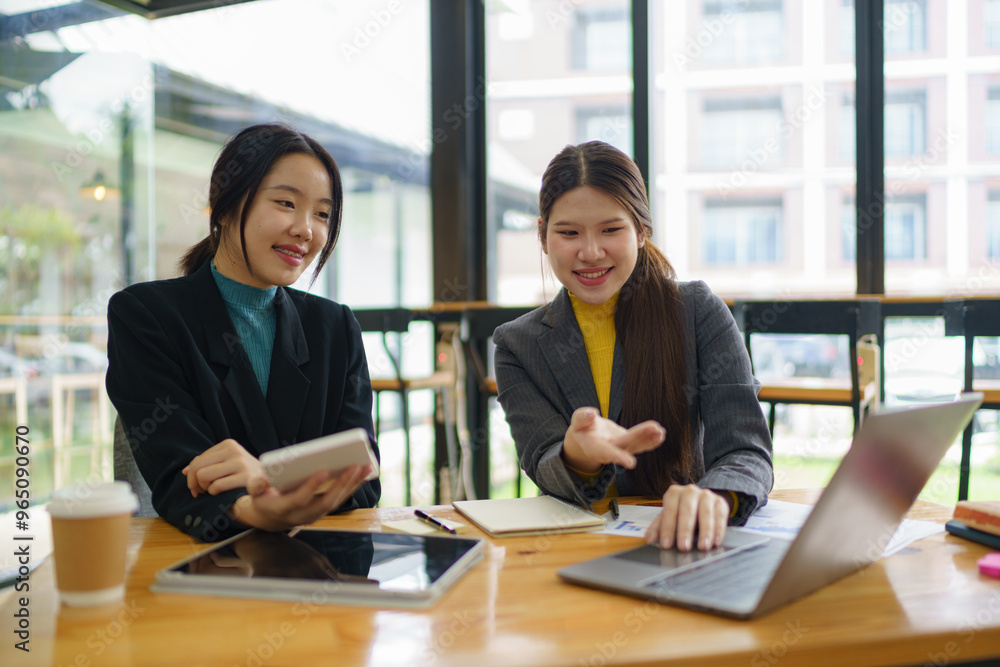 Two young Asian businesswomen discussed investment project work and planning strategy. Business people talk together on laptop computers at the office. Two young Asian businesswomen discussed investment project work and planning strategy. Business people talk together on laptop computers at the office.