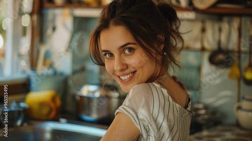 Close-up of a beautiful young woman smiling while washing dishes in the kitchen.