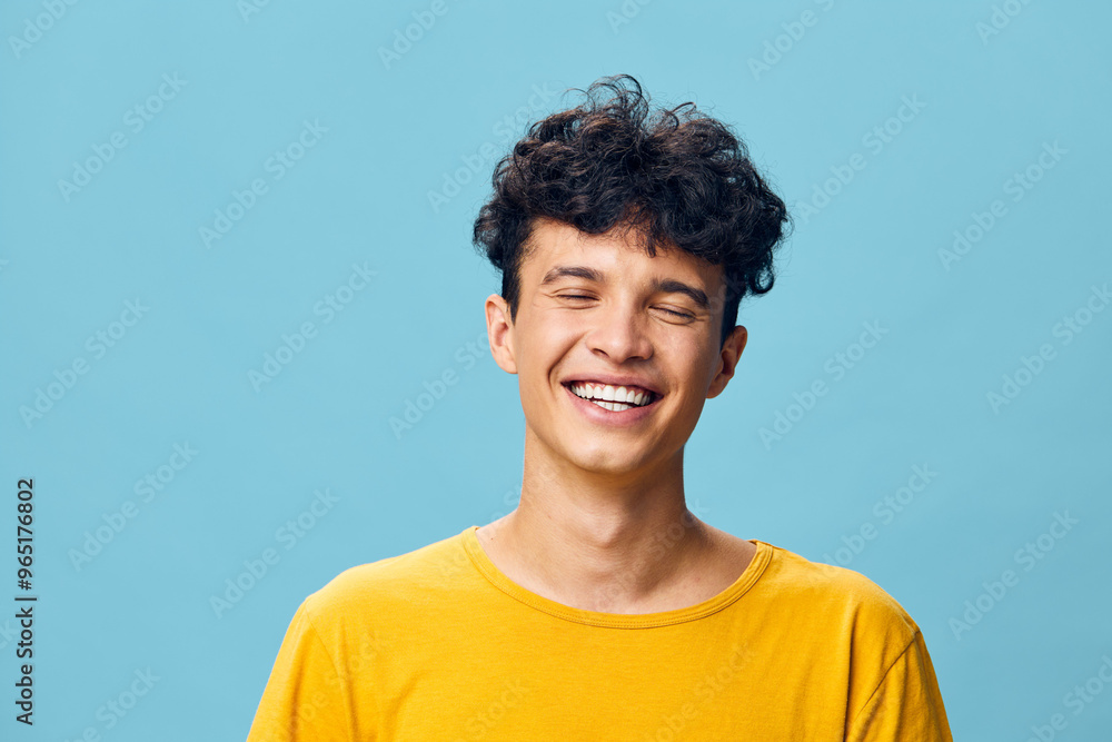 Smiling young man with curly hair wearing a yellow t shirt against a light blue background, conveying joy and positivity Close up portrait emphasizing happiness and carefree attitude Smiling young man with curly hair wearing a yellow t shirt against a light blue background, conveying joy and positivity Close up portrait emphasizing happiness and carefree attitude