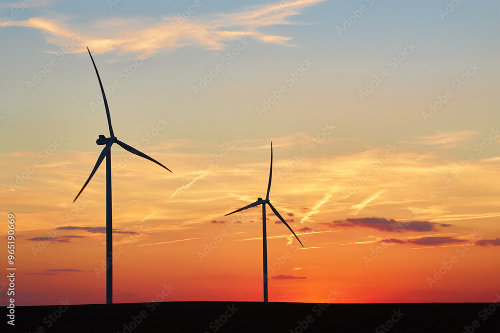 Silhouetted wind turbines in countryside landscape during sunset. Wind power plant generating clean energy. Concept of renewable and sustainable energy Silhouetted wind turbines in countryside landscape during sunset. Wind power plant generating clean energy. Concept of renewable and sustainable energy