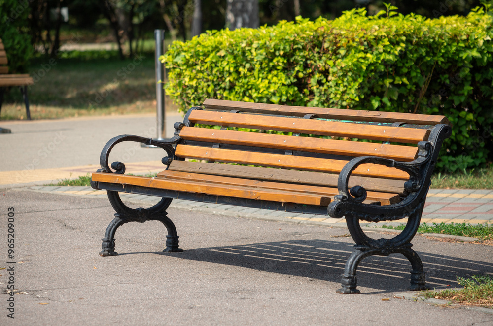 A wooden bench with black metal legs sits in a park A wooden bench with black metal legs sits in a park