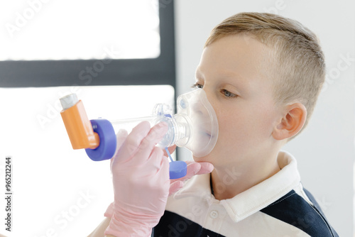 Boy with allergic asthma, inhaling his medication through spacer while sitting in doctors office