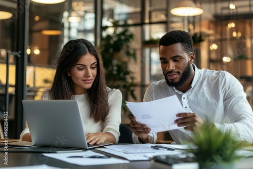 Multiethnic Entrepreneurs Working Together On A Business Plan In A Sleek Coworking Space, Reviewing Documents And Laptops