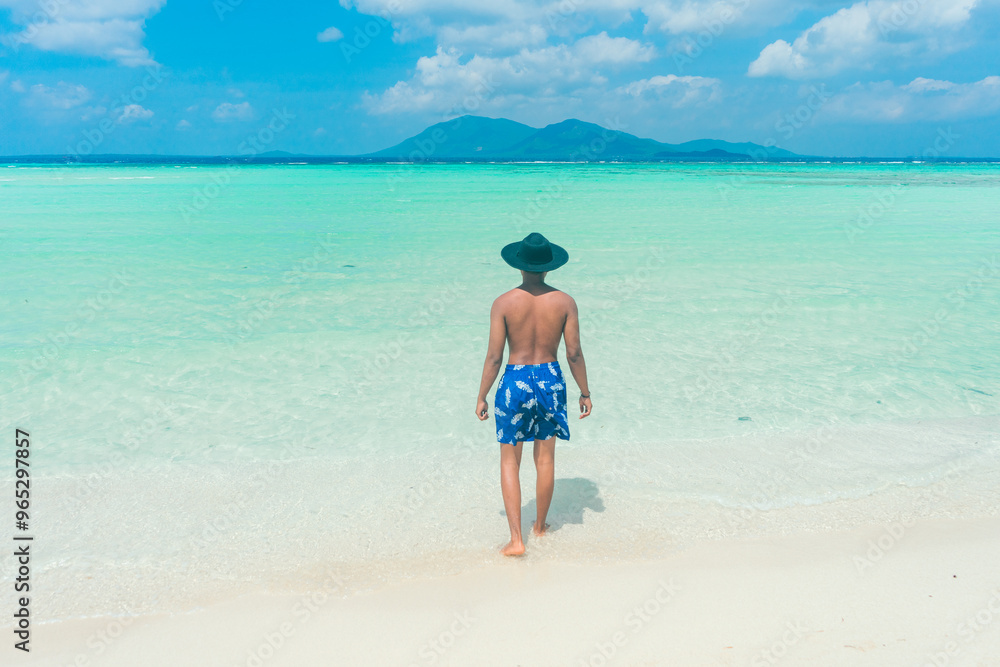 Man walking on the beach. Happy island lifestyle. White sand, blue cloudy sky and crystal sea of tropical beach. Summer vacation and summer holiday concept. Man walking on the beach. Happy island lifestyle. White sand, blue cloudy sky and crystal sea of tropical beach. Summer vacation and summer holiday concept.