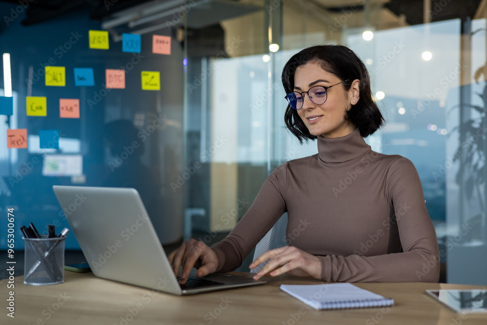 Woman working confidently on laptop in modern office setting. Focused professional in glasses using technology for business productivity. Woman working confidently on laptop in modern office setting. Focused professional in glasses using technology for business productivity.