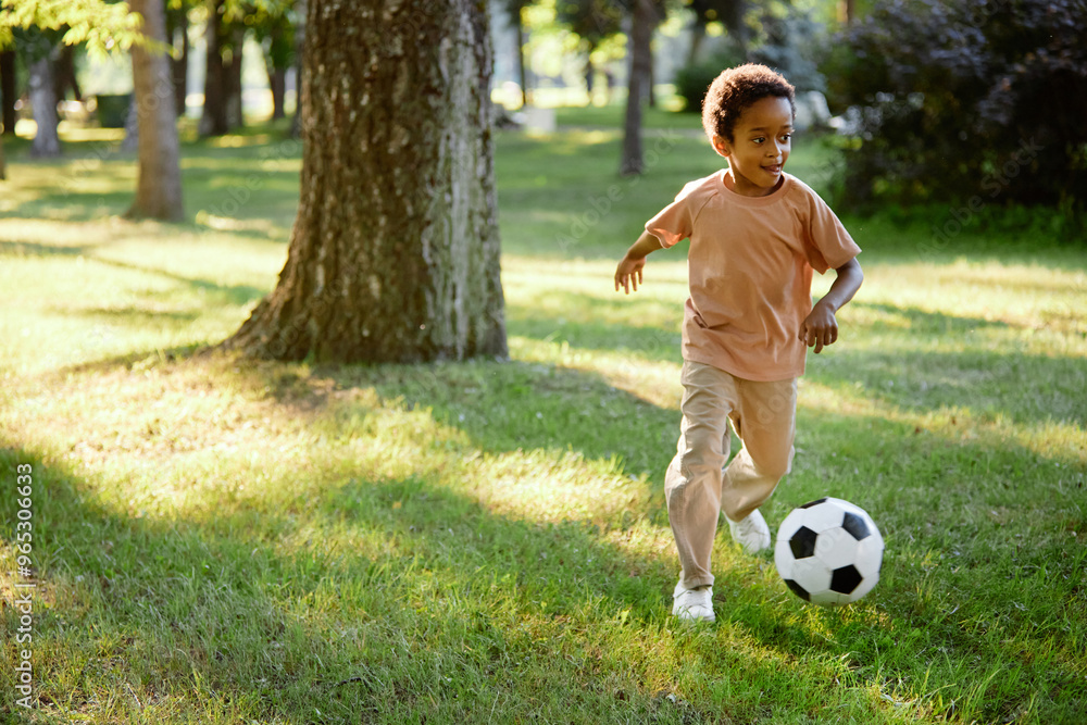 African American boy running and kicking ball while hanging out in summer park African American boy running and kicking ball while hanging out in summer park