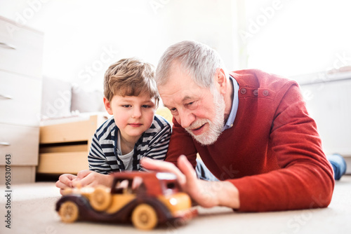 Boy and grandpa lying on floor, playing with car model. Grandfather spending time with grandson, taking care of him while parents are at work. photo