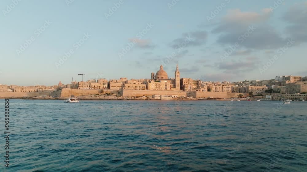 Stunning aerial shot of a historic city of Valletta (Malta) by the sea during sunset. The skyline features old architecture and domes, with boats calmly sailing on the water. (4K) Stunning aerial shot of a historic city of Valletta (Malta) by the sea during sunset. The skyline features old architecture and domes, with boats calmly sailing on the water. (4K)