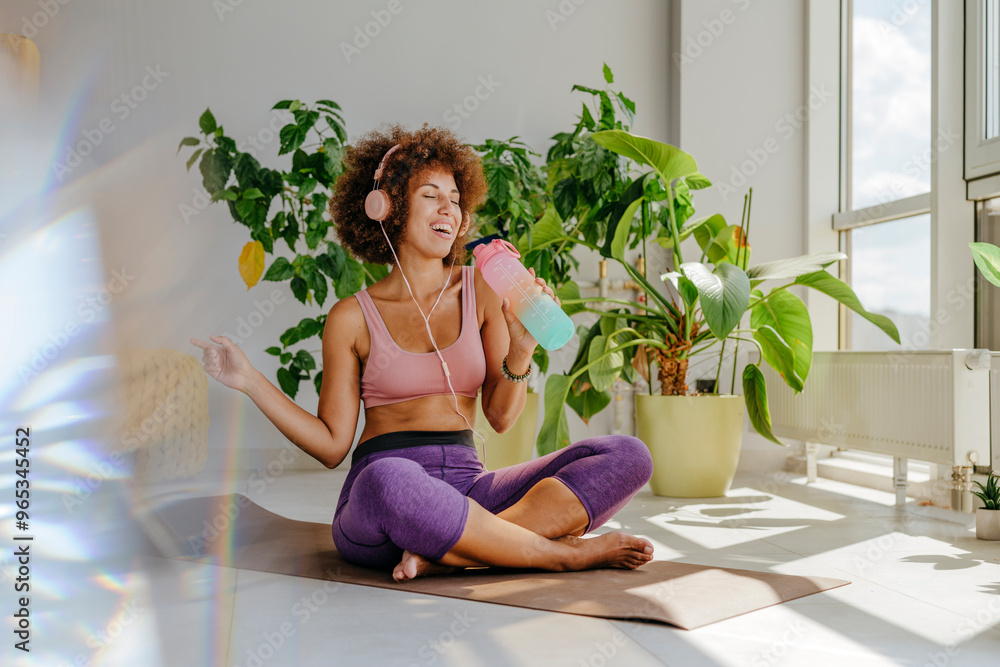 Smiling Afro woman enjoying music sitting on yoga mat at home Smiling Afro woman enjoying music sitting on yoga mat at home