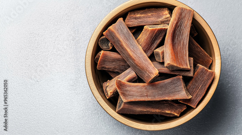 Wooden bowl filled with pieces of dried fruit leather or jerky on a textured gray background. The strips have a reddish-brown color and a leathery texture.