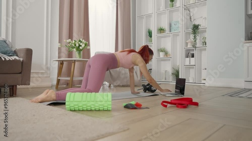 Online fitness tutorials for housewives, woman training at home, look at laptop. Healthy lifestyle and keeping fit, slender young lady training and viewing video on web site at computer screen, sports photo