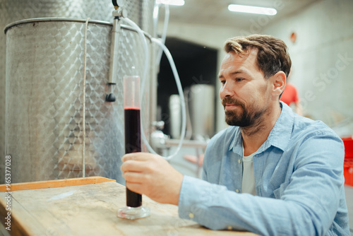 Фототапет Winemaker standing in the wine cellar, controlling, testing wine sample