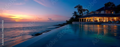 Stunning oceanfront villa at twilight, featuring a serene infinity pool and breathtaking sunset views over calm waters.