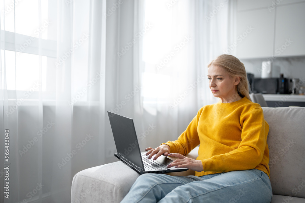 Naklejka premium A blonde woman is working with intense focus from her home office, typing on a laptop