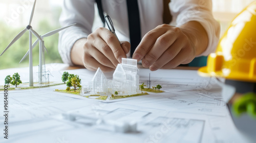 Close up of an engineers hand adjusting wind turbine model while working on architectural plans, showcasing innovation and sustainability in design