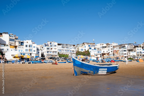 Blue boat on beach in Taghazout, Morocco. Small fishing and surfing village with sandy beach, boats and Moroccan buildings near Agadir. Popular seaside resort among surfers